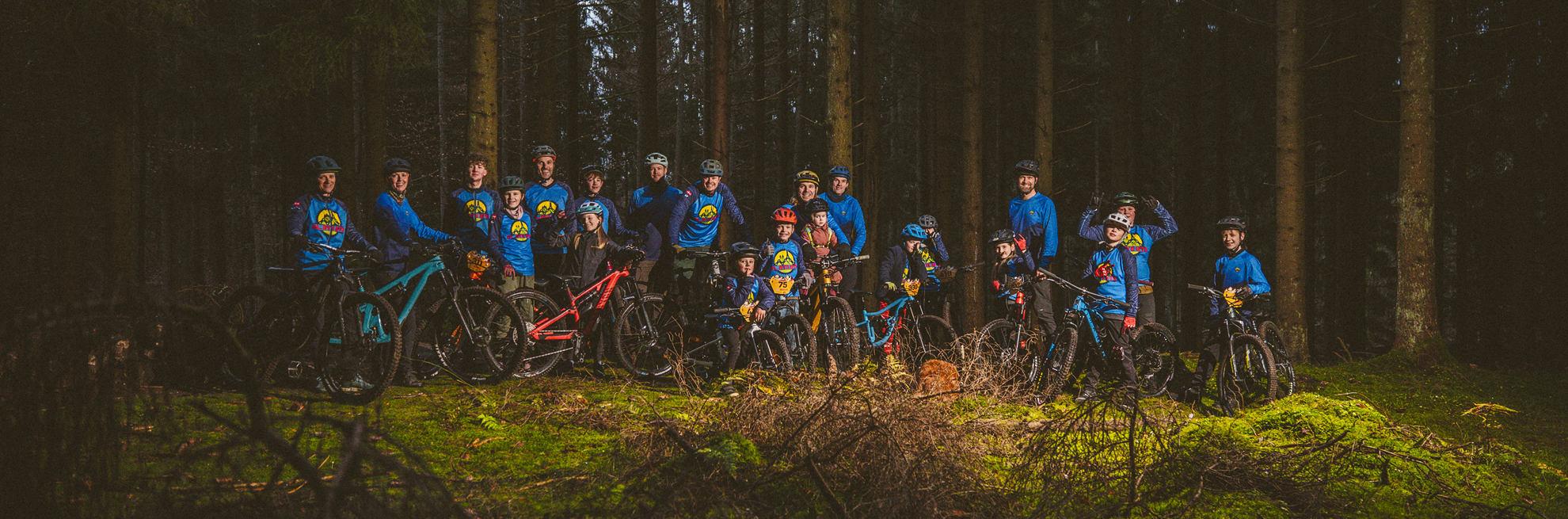 En gruppe MTB'ere med hjelm og udstyr smiler til kameraet i en skov.